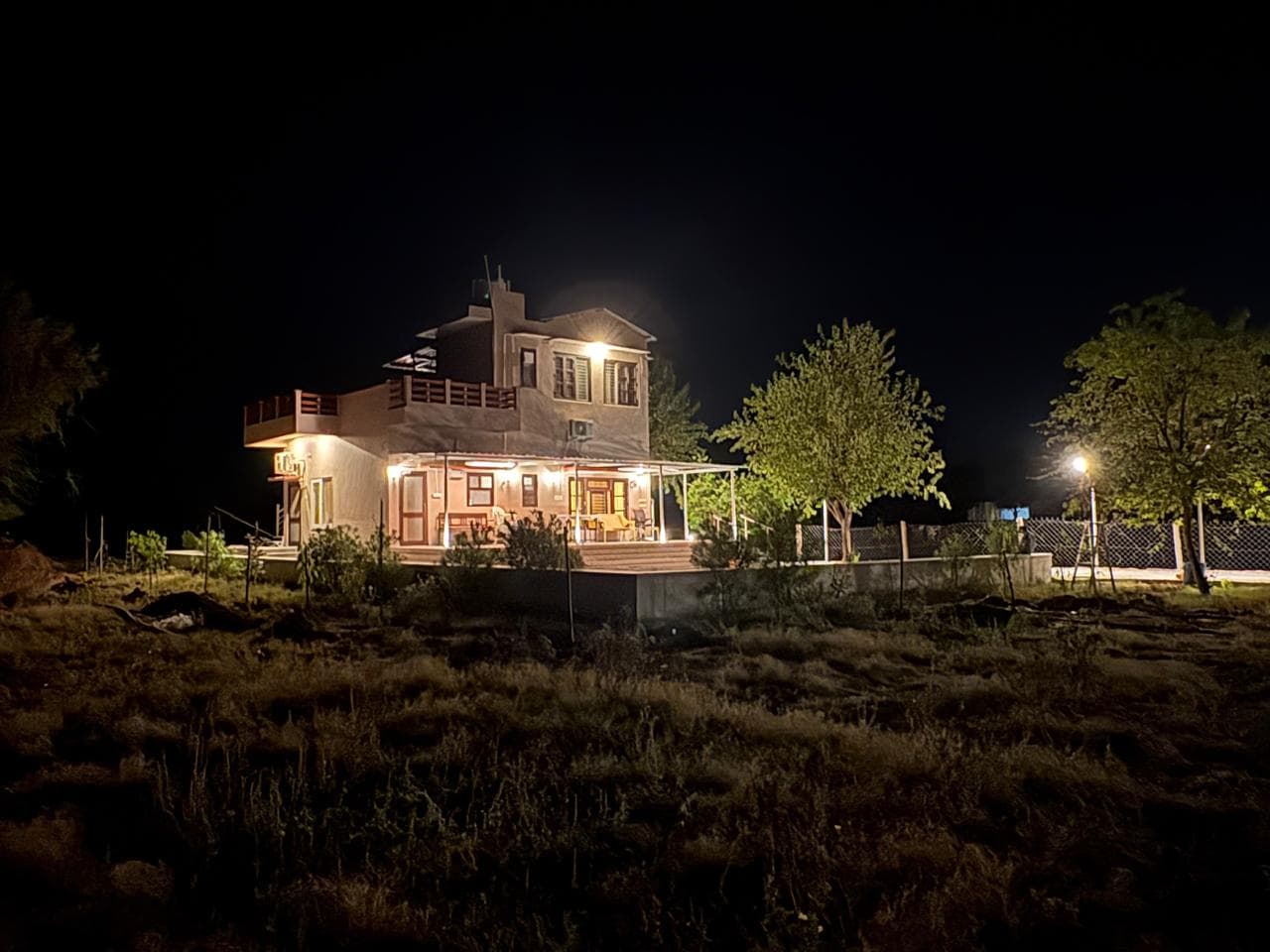 The Shiv Bagh farmhouse at dusk, its verandahs lit warm against the open countryside